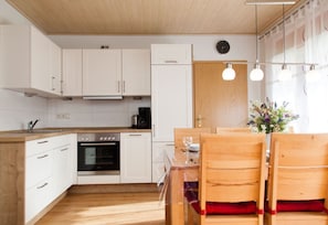 Cocina compacta con armarios blancos, horno empotrado y comedor con sillas y mesa de madera.
