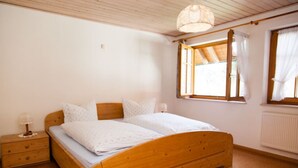 A single bed with a wooden frame, a nightstand with a lamp, and a window with curtains. - Apartment 'Ferienwohnung Schwalbennest' with Mountain View, Balcony and Wi-Fi (Mühlenbach)
