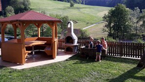 A wooden gazebo with a tiled floor, a stone oven, and a fenced area with a view of a green hillside. - Apartment 'Ferienwohnung Schwalbennest' with Mountain View, Balcony and Wi-Fi (Mühlenbach)