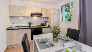 A modern kitchen with light wood cabinets, a black stove, and a dining area with a table set for two. - Apartment 'Talblick' with Mountain View, Private Terrace and Wi-Fi (Loffenau)