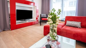A modern living room with a red sofa, a glass coffee table with a smartphone, a TV on a white entertainment unit, and a vase with flowers. - Apartment 'Talblick' with Mountain View, Private Terrace and Wi-Fi (Loffenau)