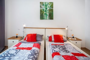 A double bed with a red and grey patterned bedspread, a nightstand with a lamp, and a wall-mounted painting.