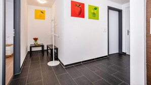 A hallway with dark tiled flooring, white walls, and two fruit paintings. - Apartment 'Talblick' with Mountain View, Private Terrace and Wi-Fi (Loffenau)