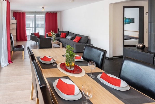 Un espace repas avec une longue table dressée pour quatre personnes, un canapé et un petit coin cuisine équipé d’une bouilloire.