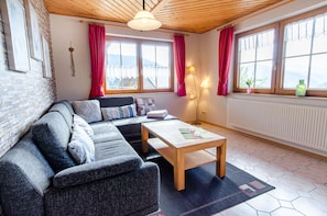 A cozy living room with a sectional sofa, a wooden coffee table, and a view of mountains through large windows.