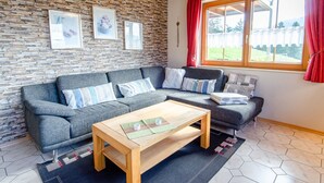 A modern living room with a stone wall, two sofas, a wooden coffee table, and a window with red curtains.