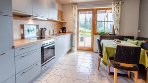 A modern kitchen with a dining area, wooden ceiling, and a view of greenery outside.