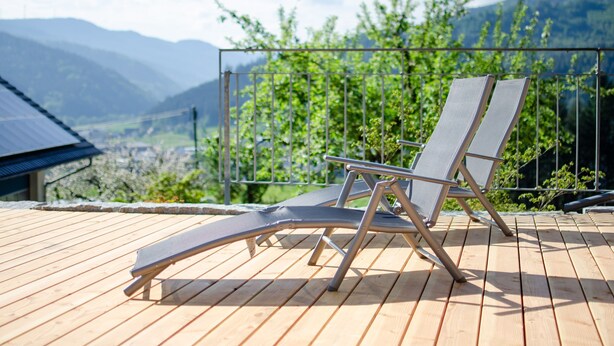 A wooden deck with two lounge chairs, a metal railing, and a view of mountains.