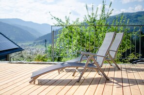 Una terraza de madera con dos sillones, una barandilla metálica y vistas a montañas.