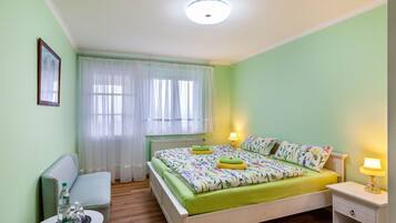 Un dormitorio con cama, mesita de noche, lámpara y una pequeña mesa con una botella y un vaso.