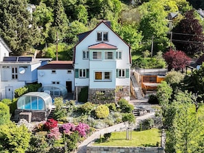 A two-story house with a red roof, surrounded by lush greenery and a garden with various plants and flowers.