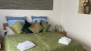 Un lit bien fait, recouvert d’une couverture verte, agrémenté de plusieurs oreillers et de serviettes pliées, le tout posé sur un plancher en bois.