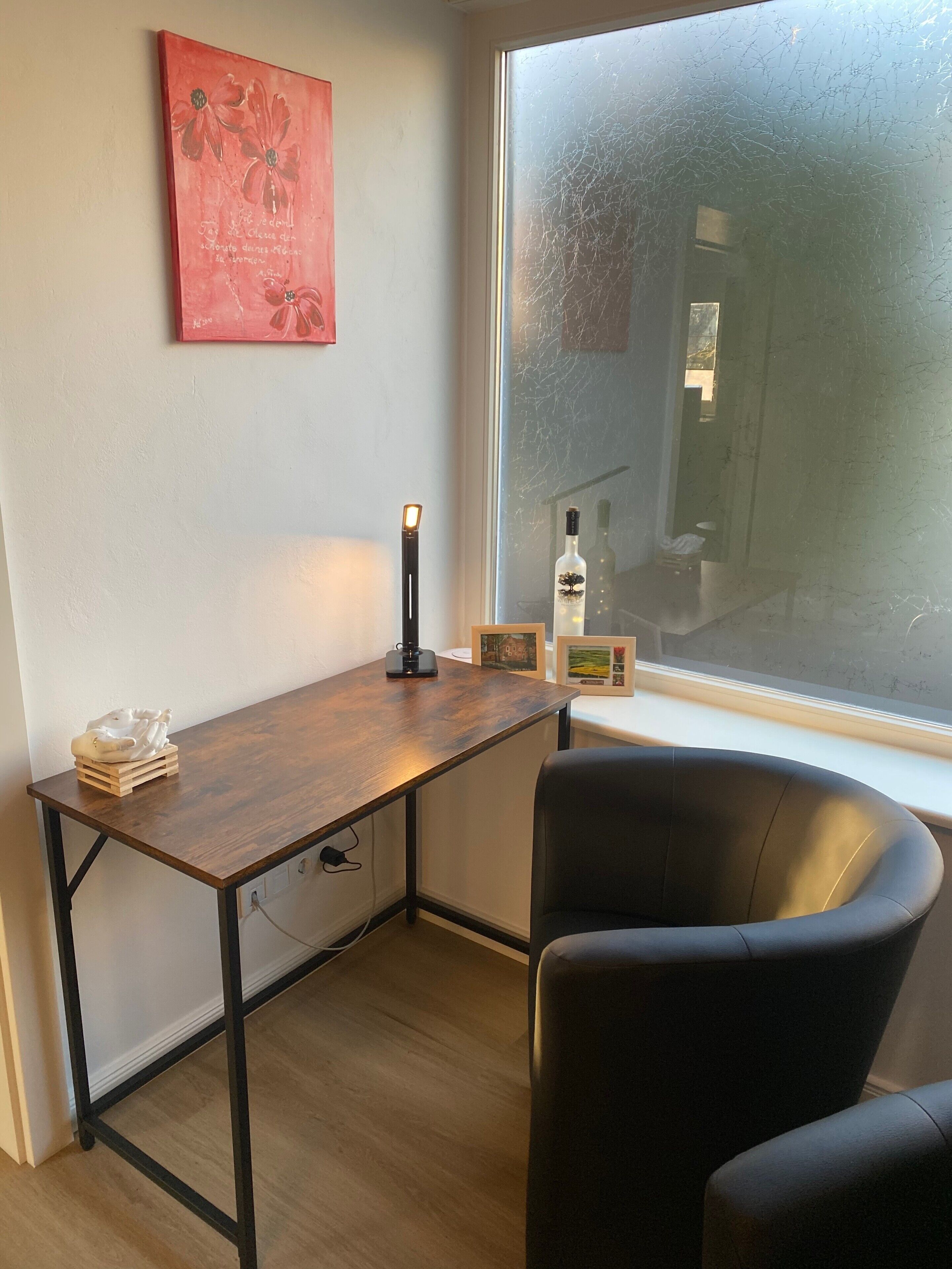 A room with a wooden desk, a black chair, a framed picture, a bottle, and a window with frost.