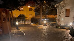 Un chemin pavé bordé de lampadaires, une entrée fermée par un portail et des bâtiments en arrière-plan.
