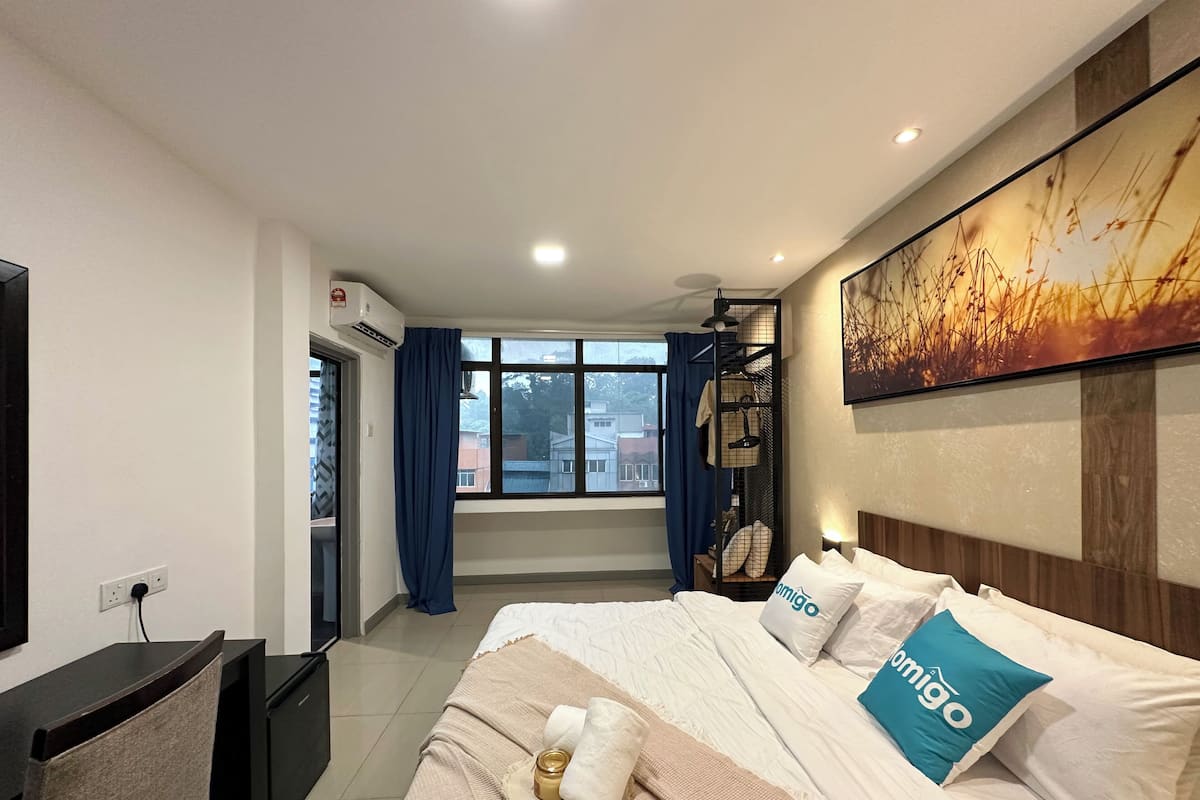 Hotellihuone, jossa on sänky, työpöytä, tuoli, televisio, ikkuna verhoilla ja taulu seinällä.