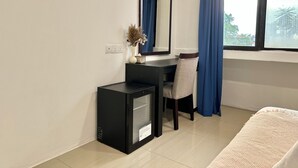 Une chambre d’hôtel de taille réduite, équipée d’un bureau, d’une chaise et d’un petit réfrigérateur noir.