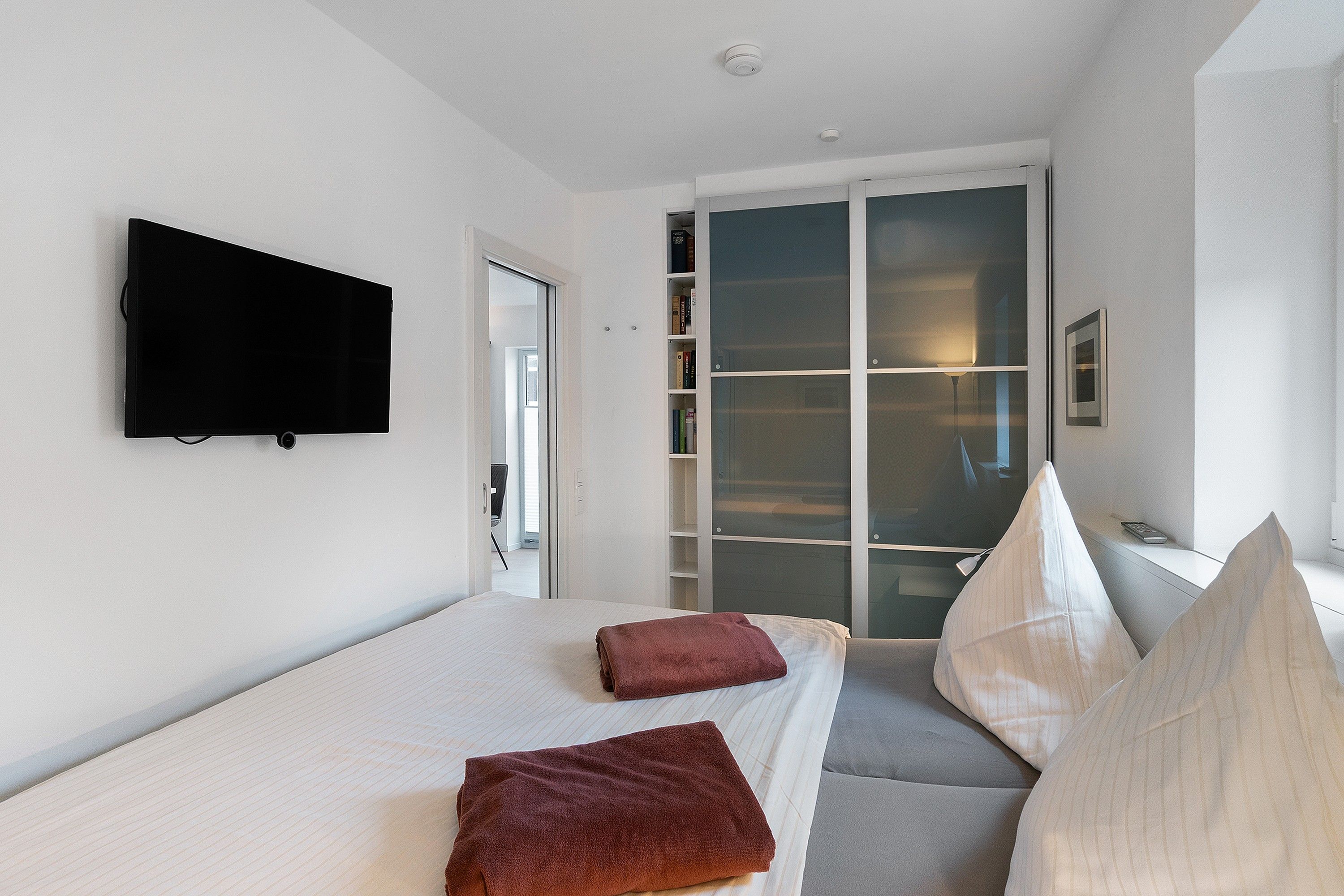 Une chambre d’hôtel moderne équipée d’un lit, d’un téléviseur à écran plat, d’une armoire à portes coulissantes et d’une table de chevet.