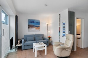 Een woonkamer met een bank, een salontafel, een stoel, een schilderij aan de muur en een boekenkast.