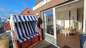 A balcony with a striped beach chair, a glass door leading to a living room with a sofa and a coffee table, and a brick wall.