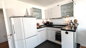 A compact kitchen with white cabinets, a black countertop, a stove, and a coffee maker.