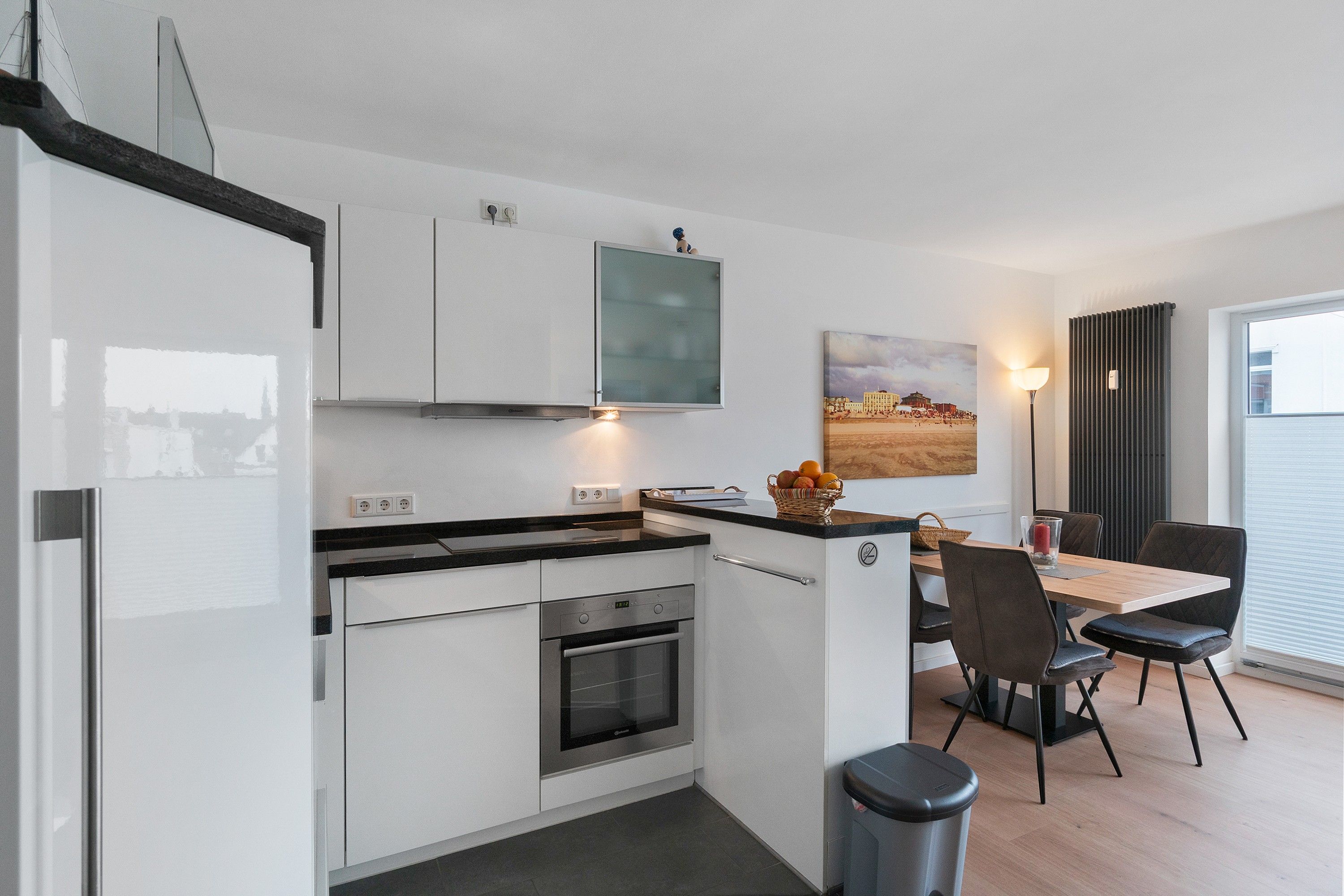 Eine moderne Küche mit weißen Schränken, einem eingebauten Backofen und einem Essbereich mit Tisch und Stühlen.