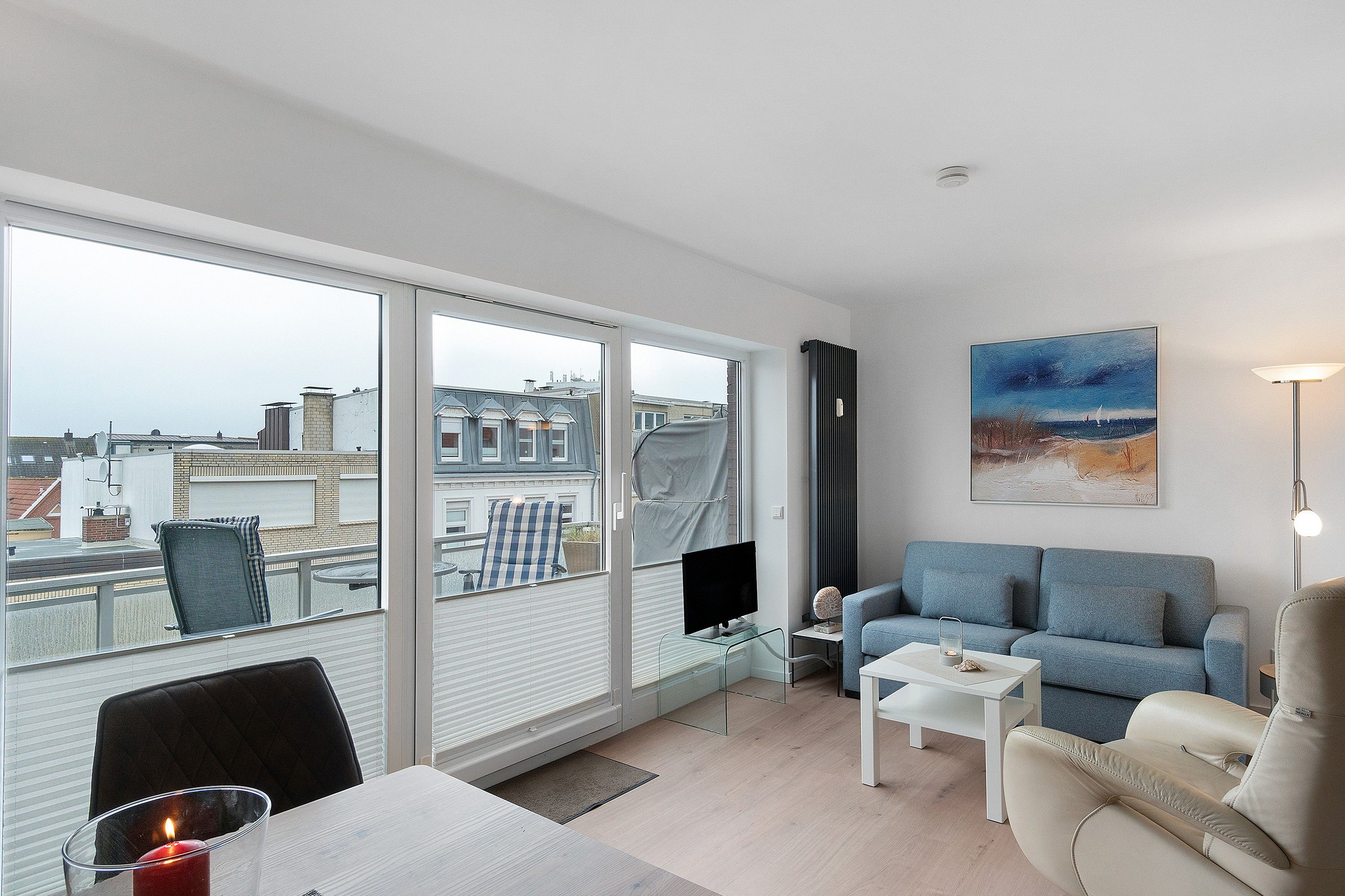 Ein modernes Wohnzimmer mit großem Fenster, einem Flachbildfernseher, einem blauen Sofa, einem weißen Couchtisch und einem Gemälde an der Wand.