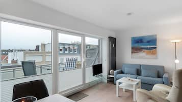 Ein modernes Wohnzimmer mit großem Fenster, einem Flachbildfernseher, einem blauen Sofa, einem weißen Couchtisch und einem Gemälde an der Wand.