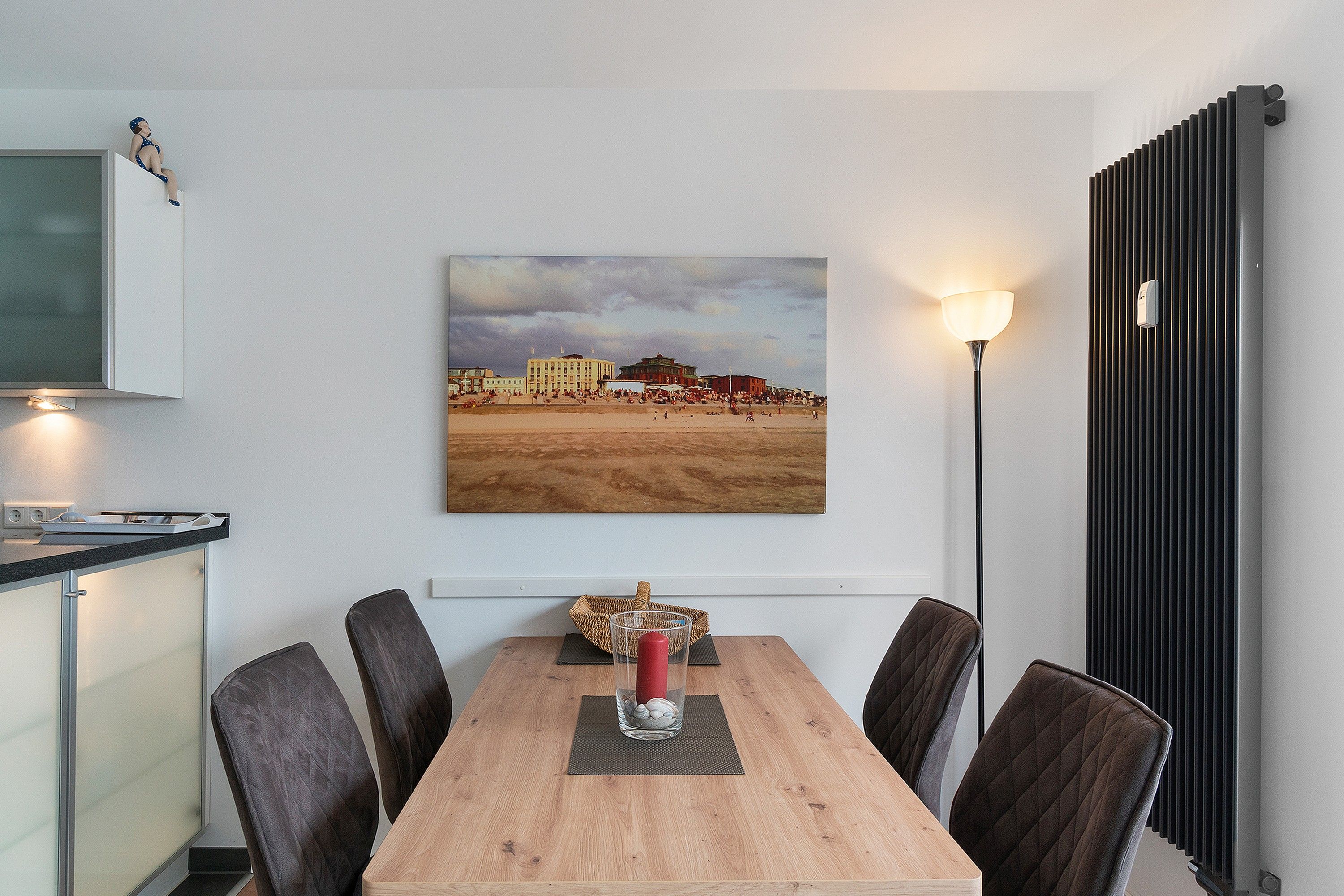 Un comedor con una mesa de madera, cuatro sillas, un jarrón con flores y un cuadro de una playa.