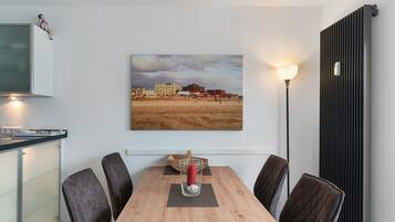Un comedor con una mesa de madera, cuatro sillas, un jarrón con flores y un cuadro de una playa.