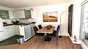 A modern kitchen with white cabinets, a wooden dining table, and a large window.