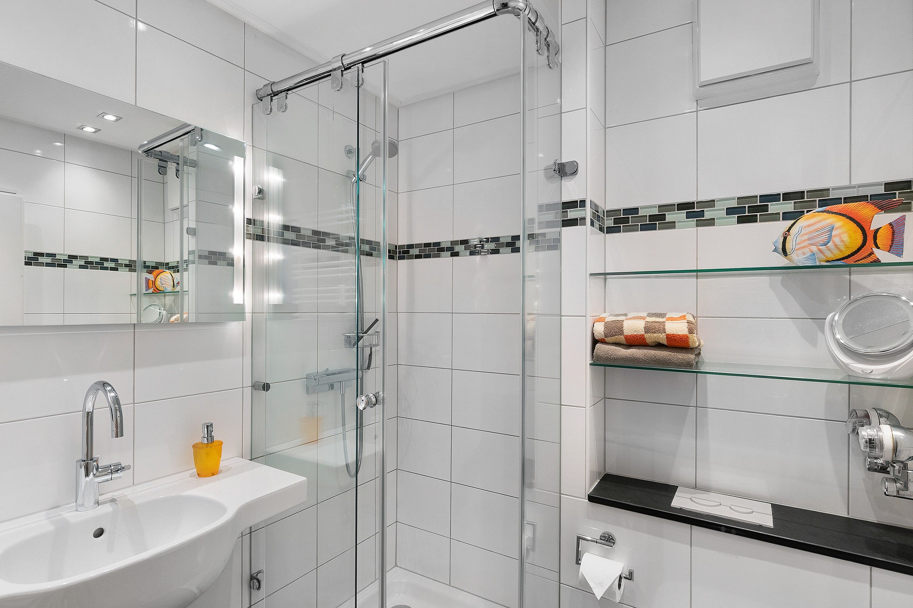 Ein modernes Badezimmer mit einer ein Glasfachwerk-Duschkabine, einem weißen Waschbecken und einer gefliesten Spritzschutzwand.
