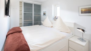 A bedroom with a bed, a nightstand, a lamp, a wardrobe, and a window with a view.
