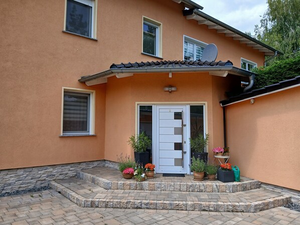 A two-story building with a white door, potted plants, and a satellite dish.