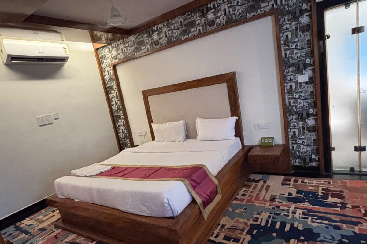 Quarto com cama grande, tapete estampado e parede com mural de paisagem urbana.