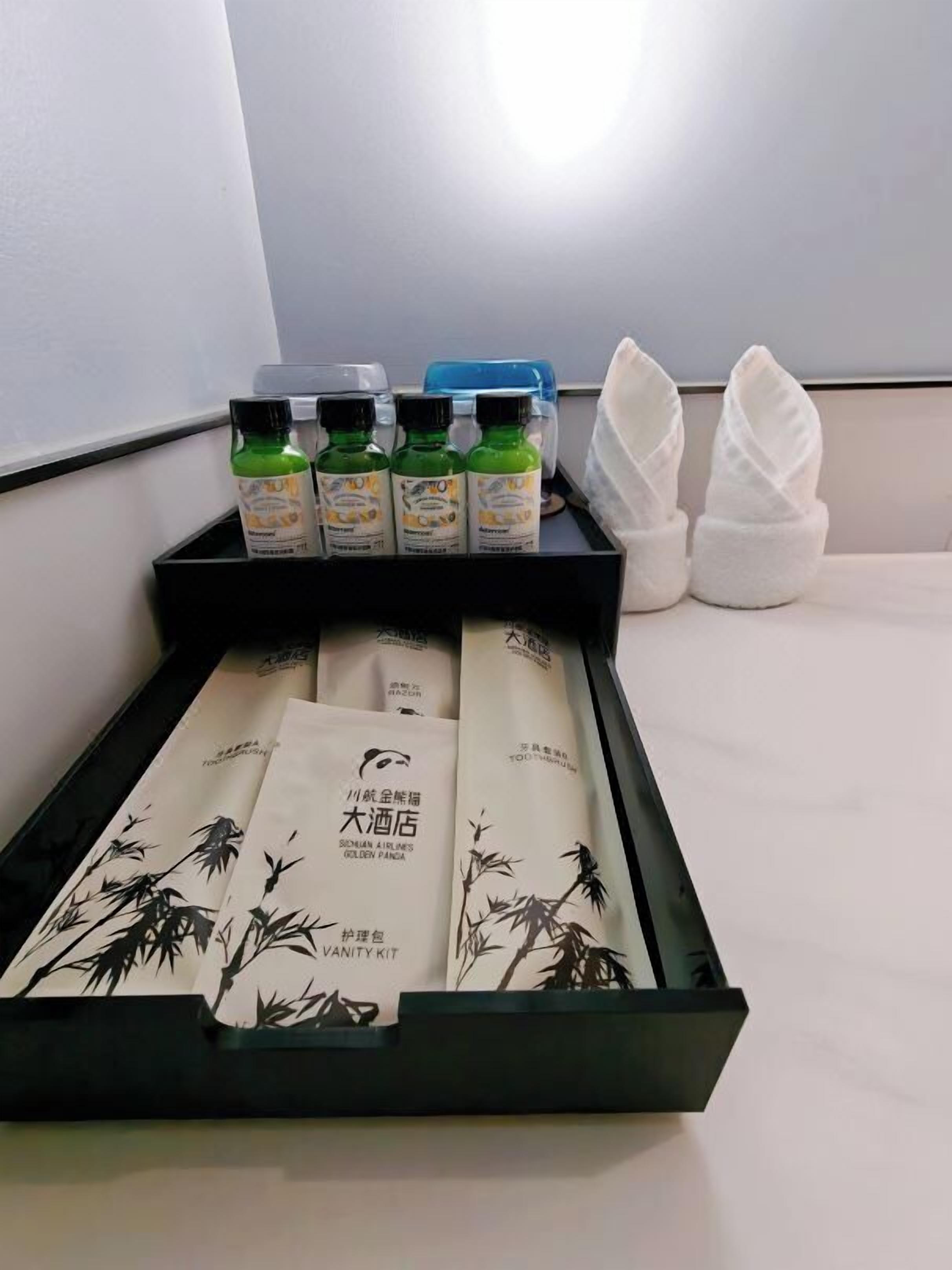 Une chambre d’hôtel avec un plateau noir contenant des bouteilles vertes, des serviettes blanches et un ensemble de produits de toilette sur le thème du bambou.
