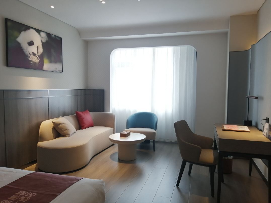 Ein modernes Hotelzimmer mit einer Couch, einem Sessel, einem Schreibtisch und einem großen Fenster.