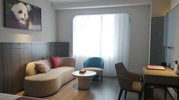 Ein modernes Hotelzimmer mit einer Couch, einem Sessel, einem Schreibtisch und einem großen Fenster.