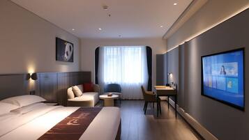 A modern hotel room with a large bed, a desk, a chair, and a television on the wall.