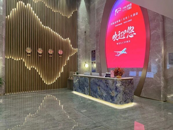 A hotel reception area with a modern design, featuring a reception desk, a digital welcome screen, and a decorative wall with vertical lines. - Golden Panda Hotel (Beijing)