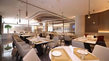 A modern restaurant with round tables, white chairs, and pendant lighting.