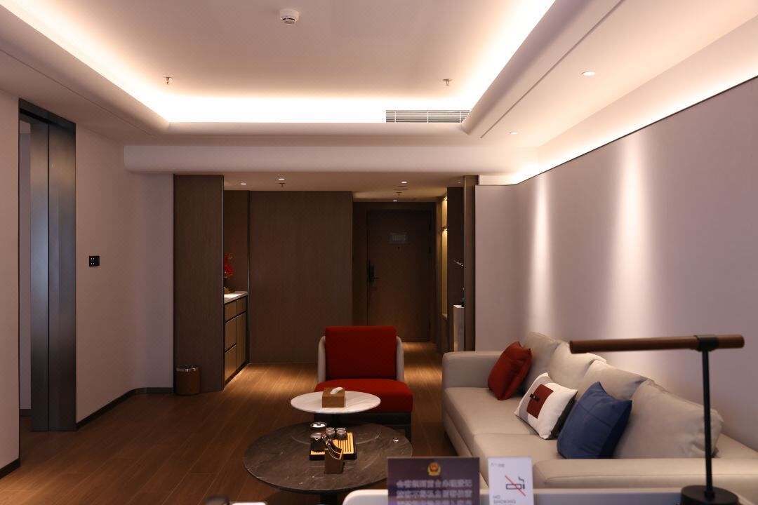 A modern hotel room with a sofa, a red chair, a coffee table, and a small dining table.