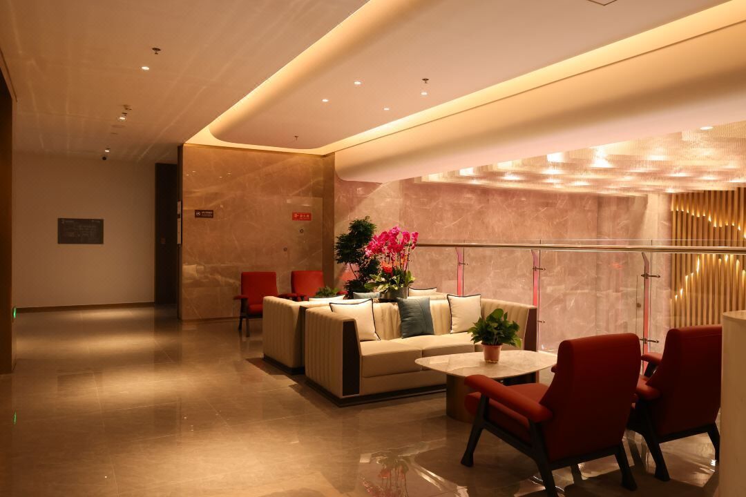 A modern lobby with a sofa, red chairs, a small table, and a potted plant.