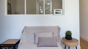 Une pièce avec une grande fenêtre, un canapé agrémenté de coussins à motifs, une petite table et une plante en pot.
