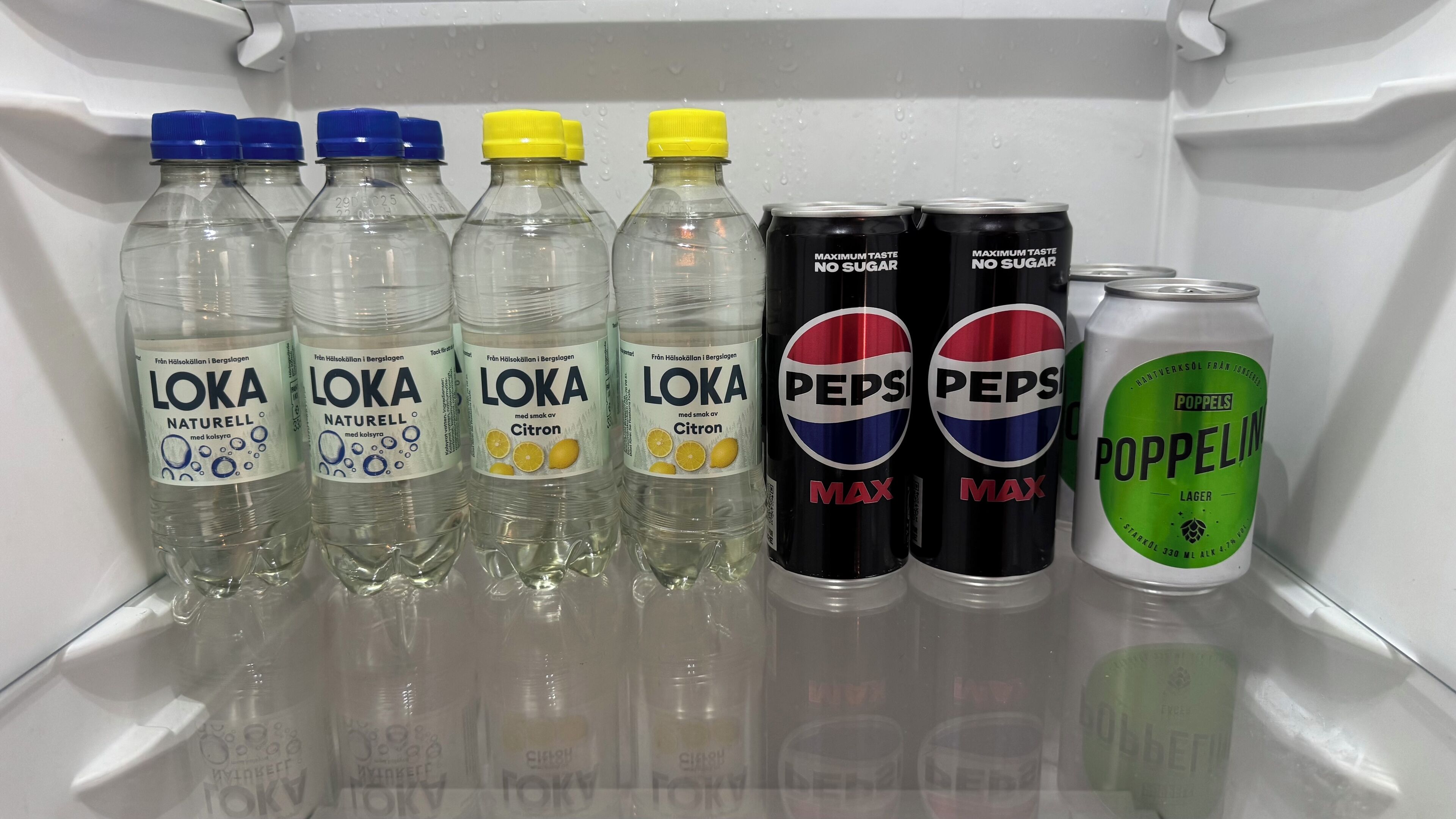 A refrigerator containing various beverages including LOKA Naturell, Pepsi Max, and Poppels Poppels.