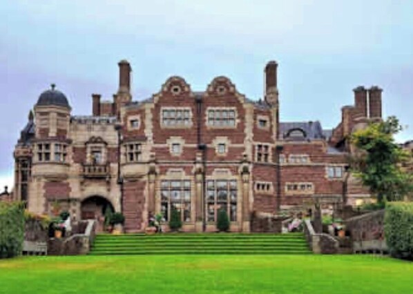 A large, historic building with a symmetrical facade, multiple chimneys, and a central entrance with steps leading up to it.