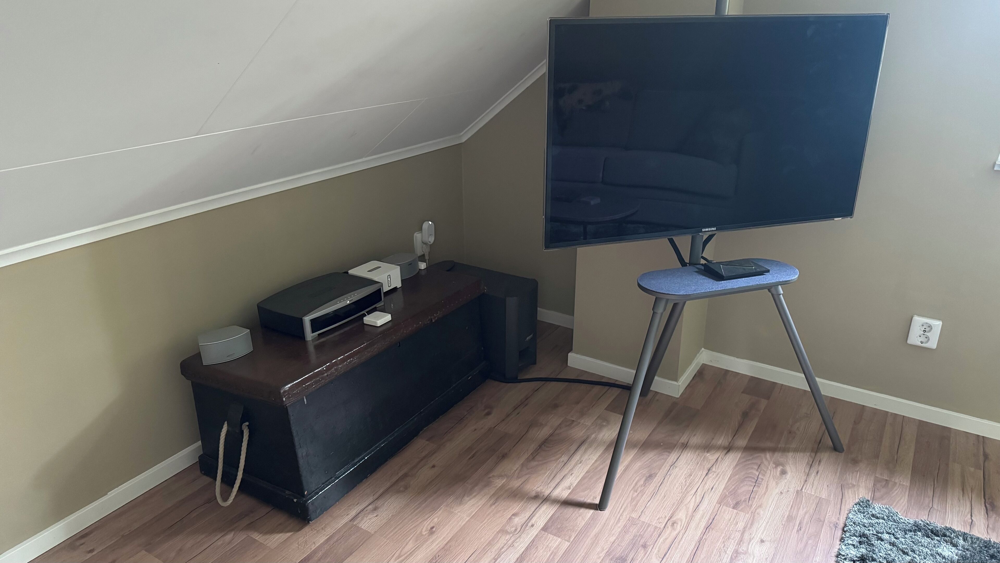 A room with a flat-screen TV on a stand, a wooden cabinet with electronic devices, and a carpeted floor.
