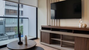 Una sala de estar moderna con un televisor grande montado en una pared de madera, una mesa redonda de centro con objetos decorativos y vistas de la ciudad a través de grandes ventanales.