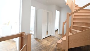 Amplia habitación con una escalera de madera, un armario y un ventanal grande.