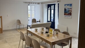 Un comedor con una mesa de madera y sillas color beige, una ventana con cortinas y una puerta con marco azul.