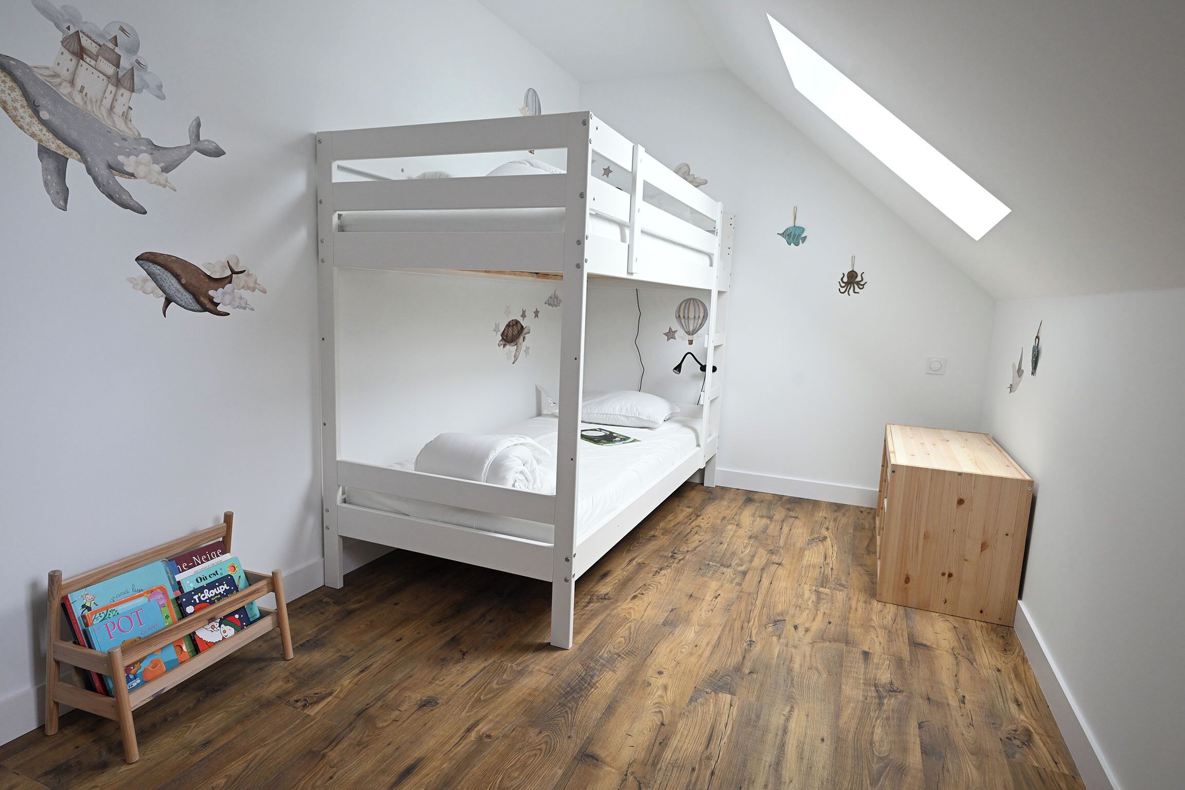 A bunk bed in a room with wooden flooring, a small wooden cabinet, and wall decorations including a whale and a hot air balloon.